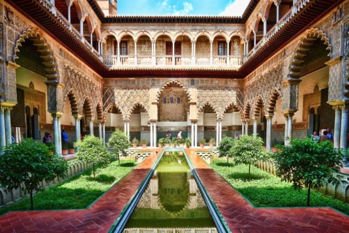 a large brick building with grass and trees with Alcázar of Seville in the background