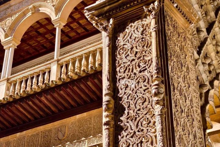 Intricate architectural detail on a column with arches and ornate carvings against a blue sky.