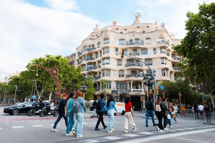a group of people walking down the street with Casa Milà in the background