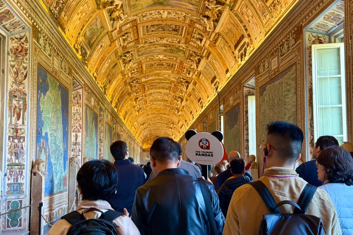 Group of tourists in a decorated corridor with an ornate ceiling.