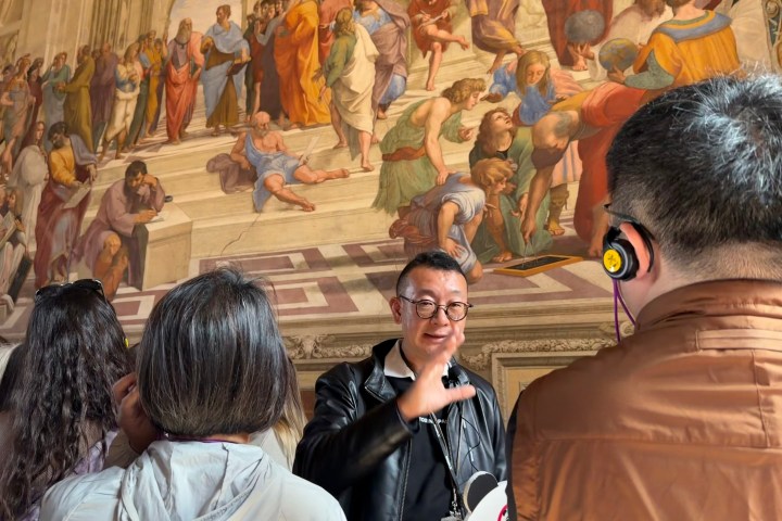 Tour guide gestures at Raphael fresco to attentive group in museum.