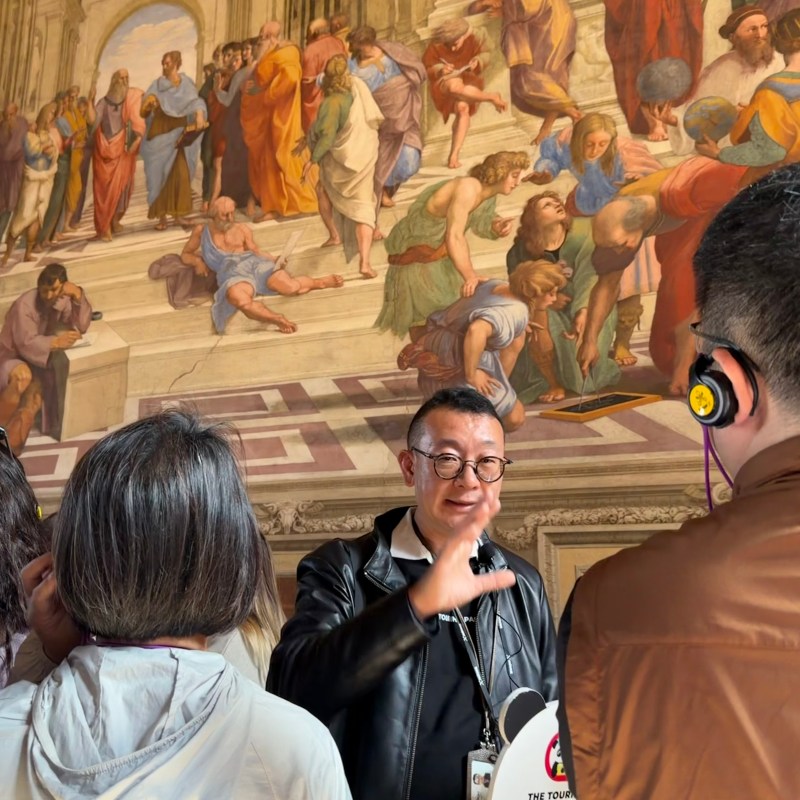 Tour guide gestures at Raphael fresco to attentive group in museum.
