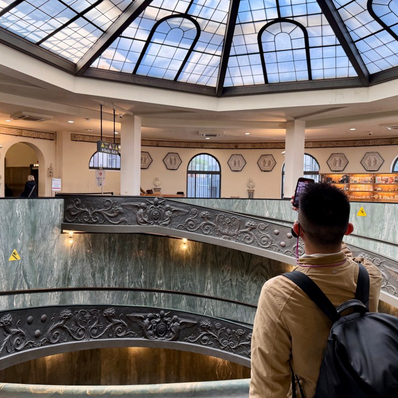 Person with backpack viewing ornate interior under skylight in a historic building.