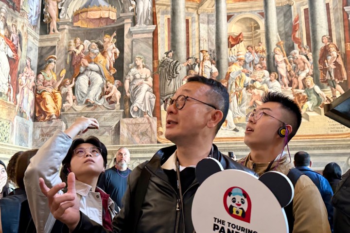 Tourists admire ornate paintings in a historic building with a sign reading 'The Touring Pandas.'