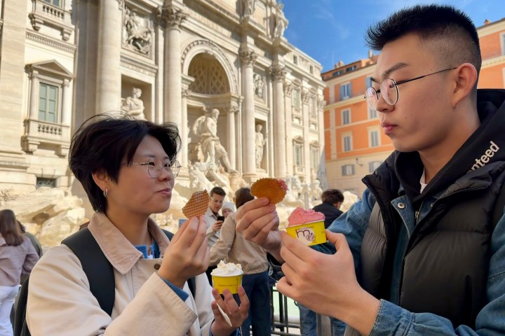 Two people enjoying gelato near the Trevi Fountain in Rome on a sunny day.