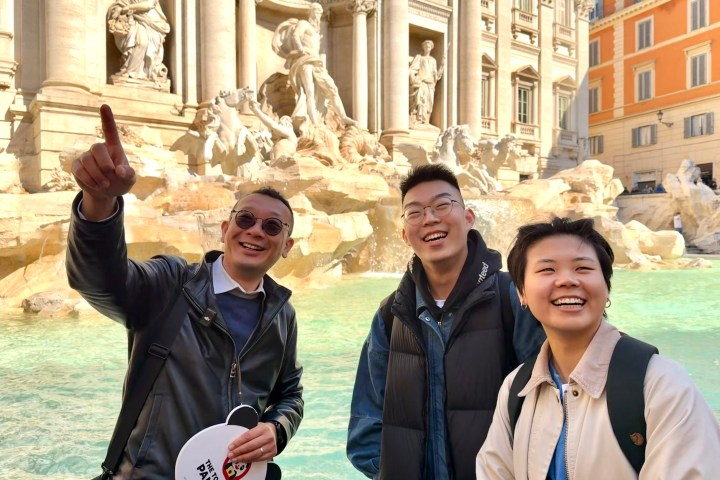Three people smiling near the Trevi Fountain on a sunny day.