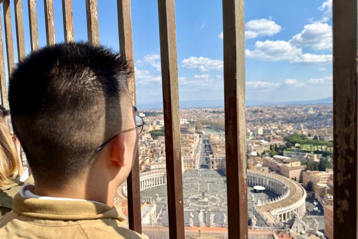 Person looking through bars at a cityscape with blue sky and clouds.
