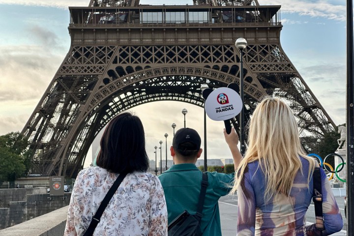 Three people stand near the Eiffel Tower, one holding a 'Touring Pandas' sign.