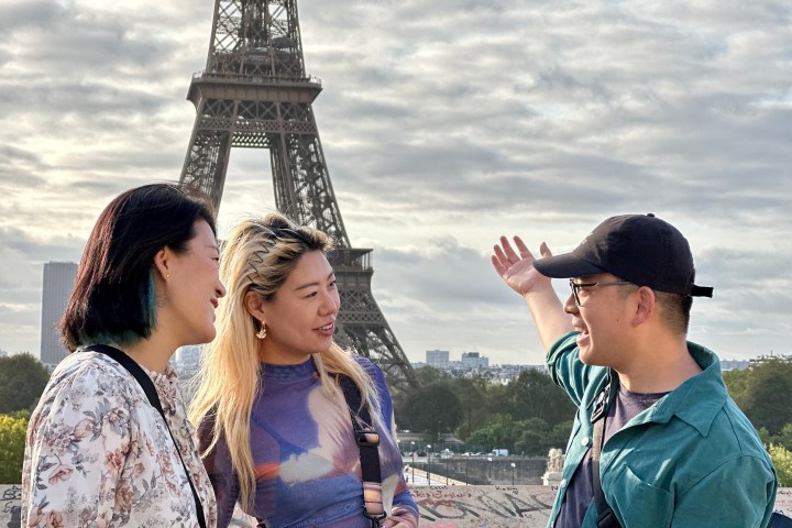 Three people smiling near Eiffel Tower on a cloudy day.