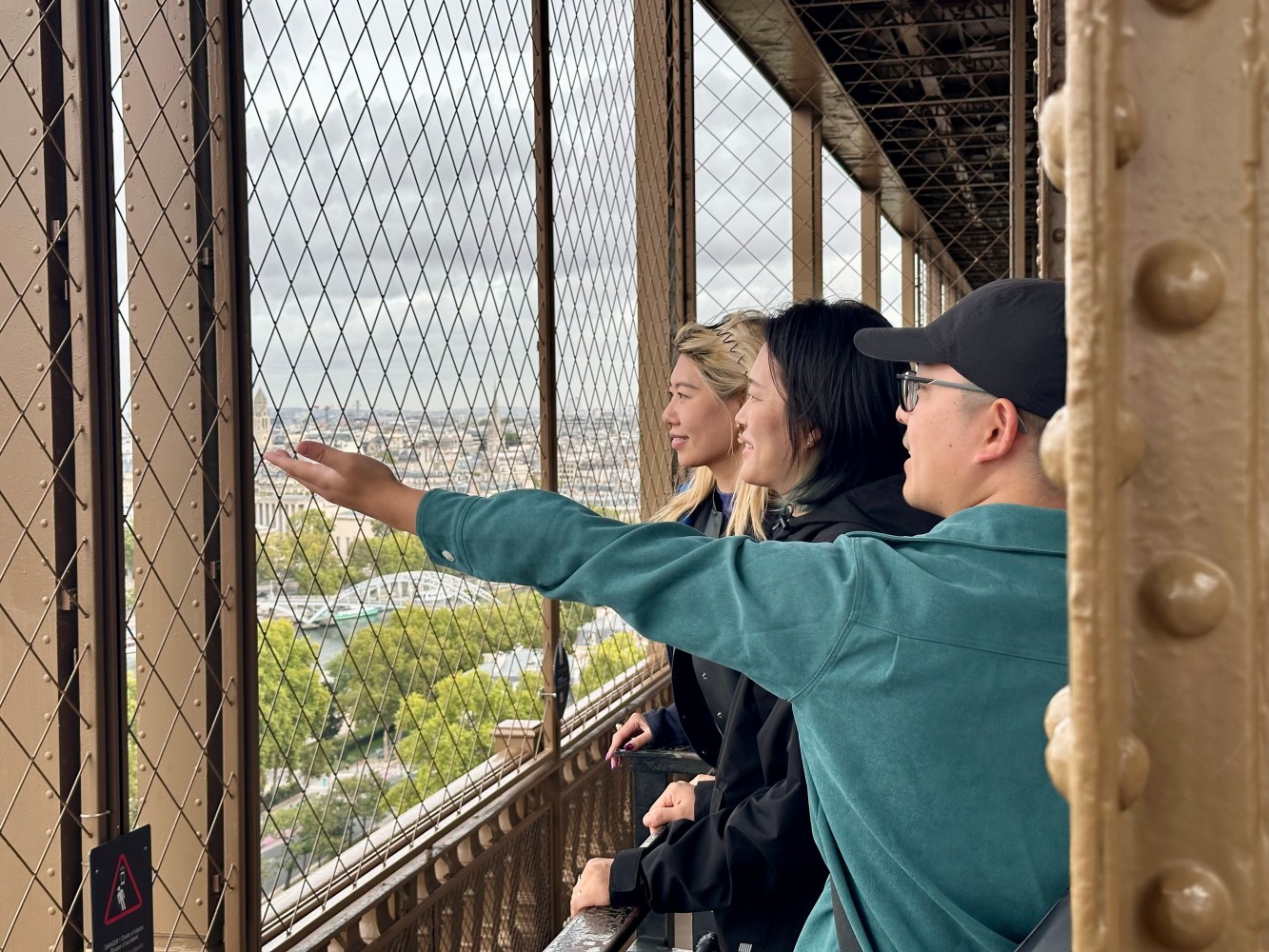 Three people looking out from an Eiffel Tower observation deck behind a metal safety grid.