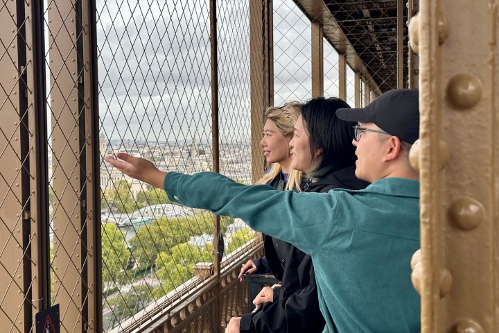 Three people looking out from an Eiffel Tower observation deck behind a metal safety grid.