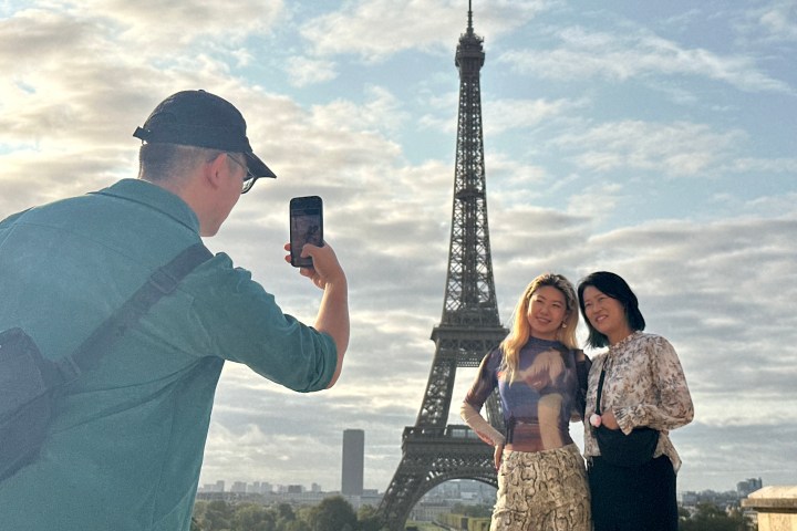 Man taking a photo of two women posing with the Eiffel Tower in the background.