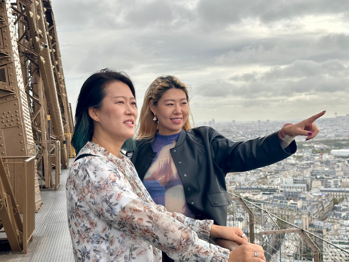 Two people on the Eiffel Tower viewing platform, one pointing at the skyline.