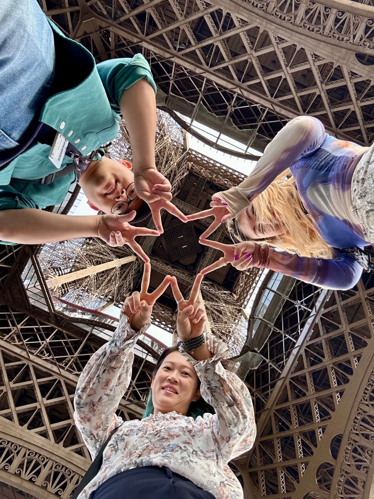 Three people forming a star shape with their fingers under the Eiffel Tower.