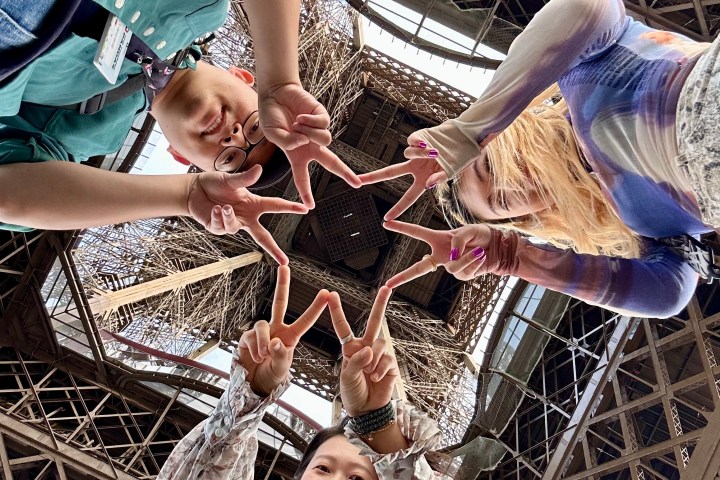 Three people forming a star shape with their fingers under the Eiffel Tower.