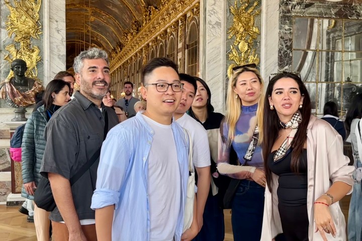 Group of people in ornate hall with gold decorations and large mirrors.
