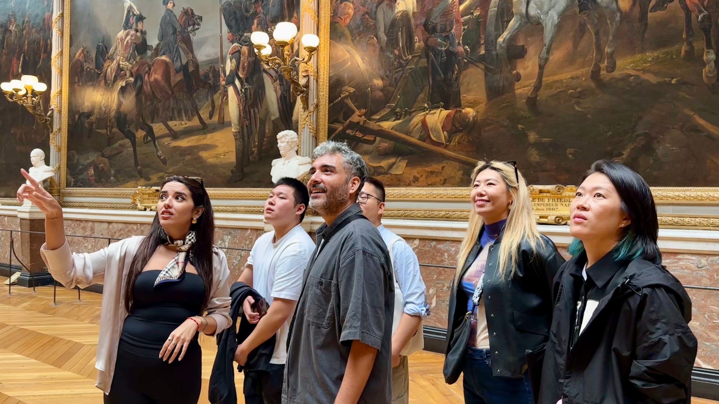 Group of people admiring large historical paintings in an art gallery.