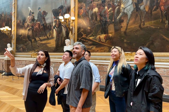Group of people admiring large historical paintings in an art gallery.