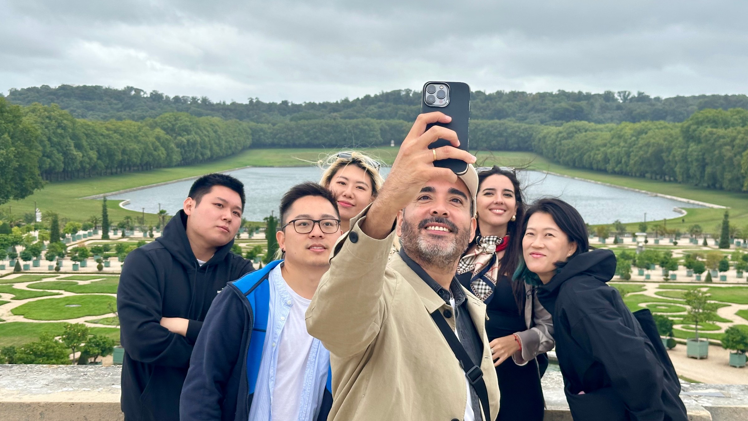 Group of six people taking a selfie with a formal garden and water feature in the background.