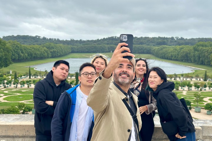 Group of six people taking a selfie with a formal garden and water feature in the background.