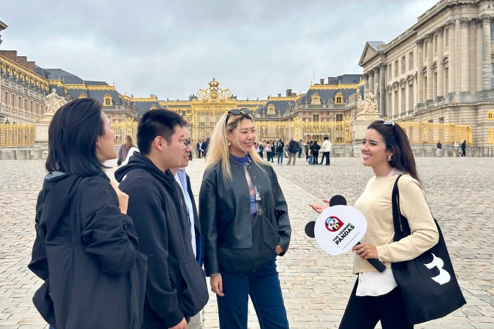 Four people talking in front of an ornate building with golden gates.