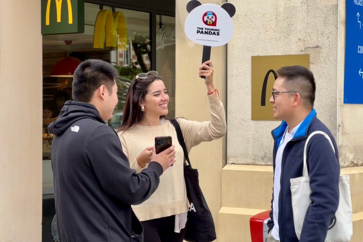 Three people outside a McDonald's; woman holds a sign, others holding smartphones and wearing casual clothes.