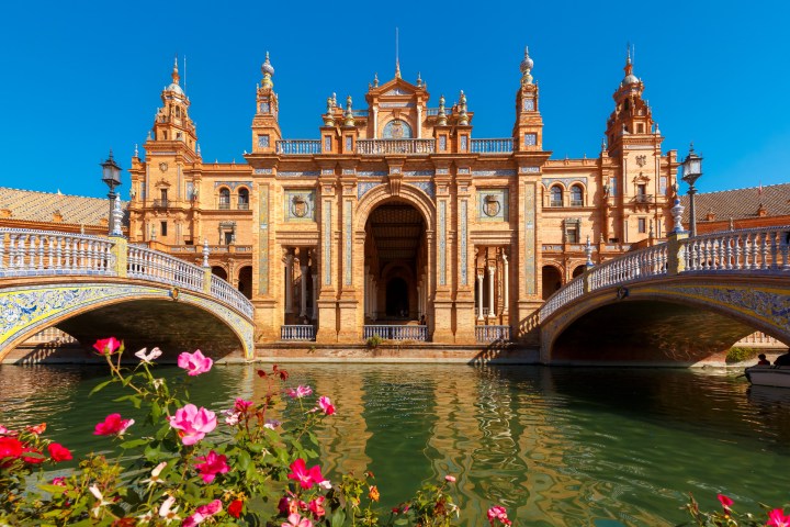 Ornate building with bridges over water, framed by vibrant flowers.