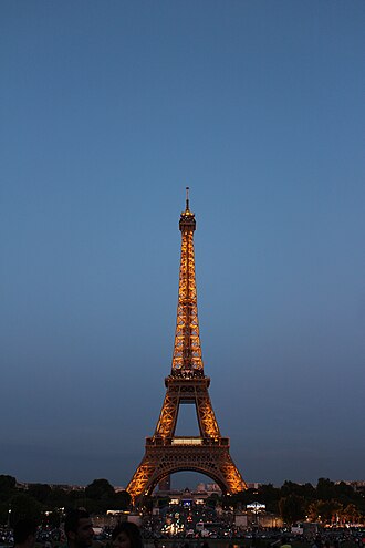 Eiffel Tower illuminated at dusk against a clear blue sky.