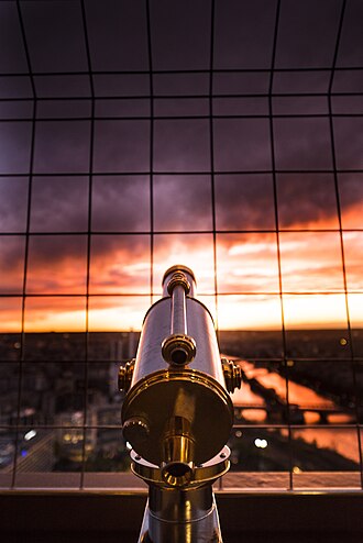 Telescope facing a sunset view through a metal safety grid.