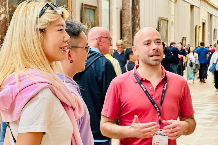 Group of people in an art gallery, one talking, with paintings on the wall in the background.