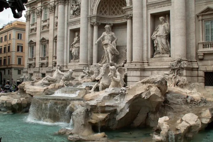 Ornate fountain with statues and cascading water in a historic city plaza.