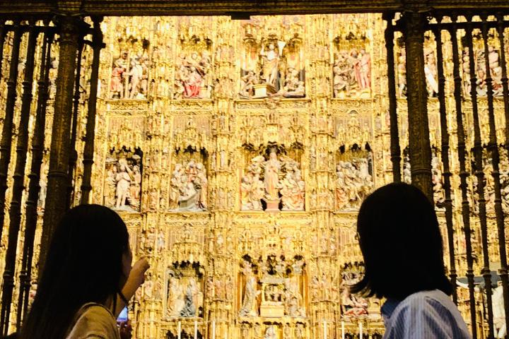 People viewing ornate golden altar with intricate religious figures and carvings.