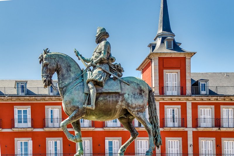 Equestrian statue in front of a red building with white windows and a spire.