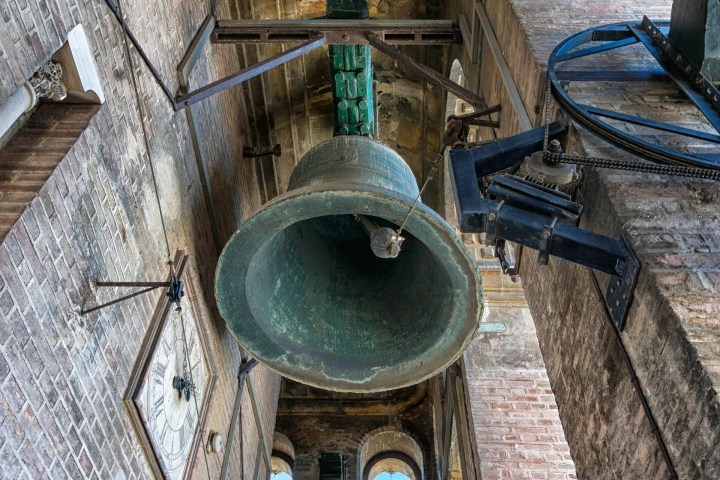 Looking up at a large green bell in a clock tower of Giralda Seville, surrounded by bricks and machinery.