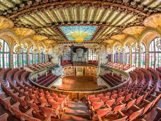 Ornate concert hall with stained glass ceiling, red seats, and decorative arches.