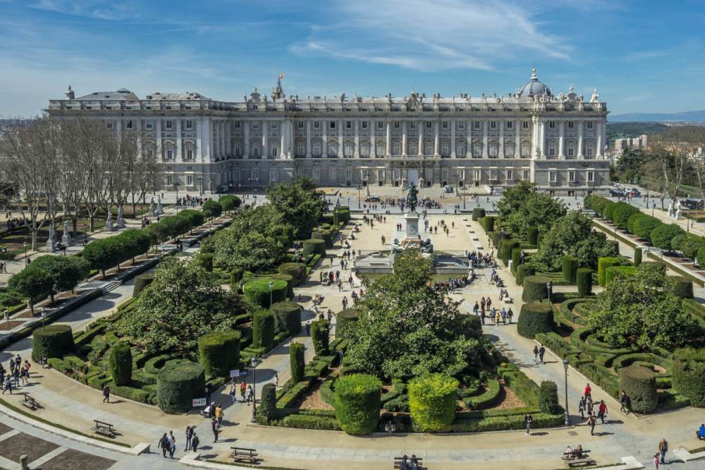 Aerial view of a large palace with formal gardens and many visitors.