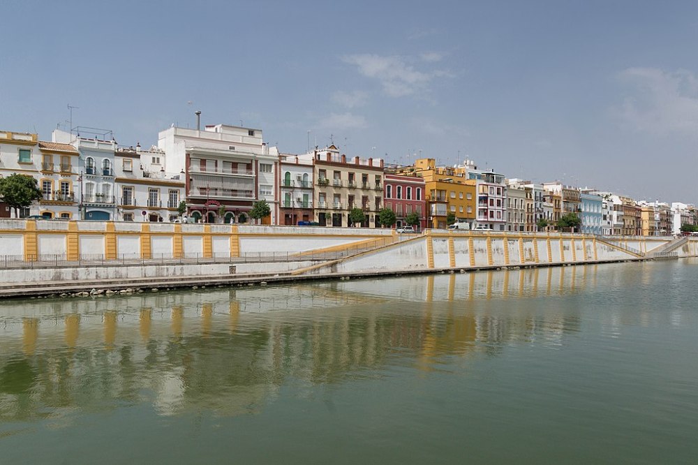 Colorful buildings line a riverside promenade, reflecting in the calm water below.