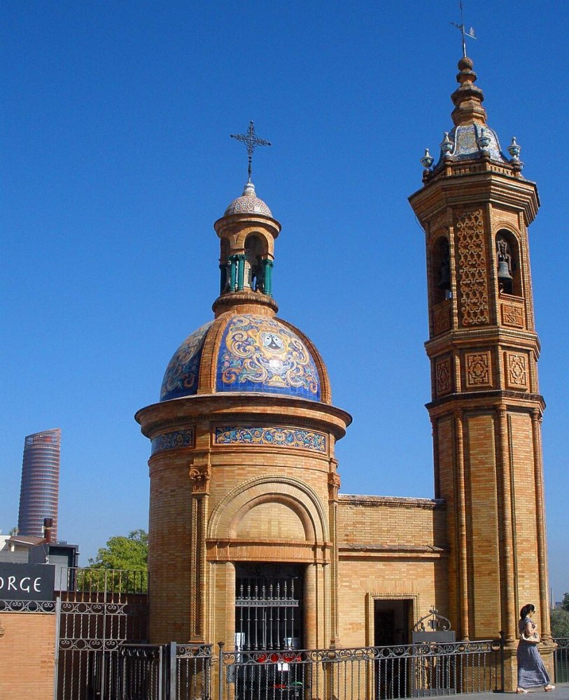 Ornate brick church with blue-tiled dome and bell tower under a clear blue sky.