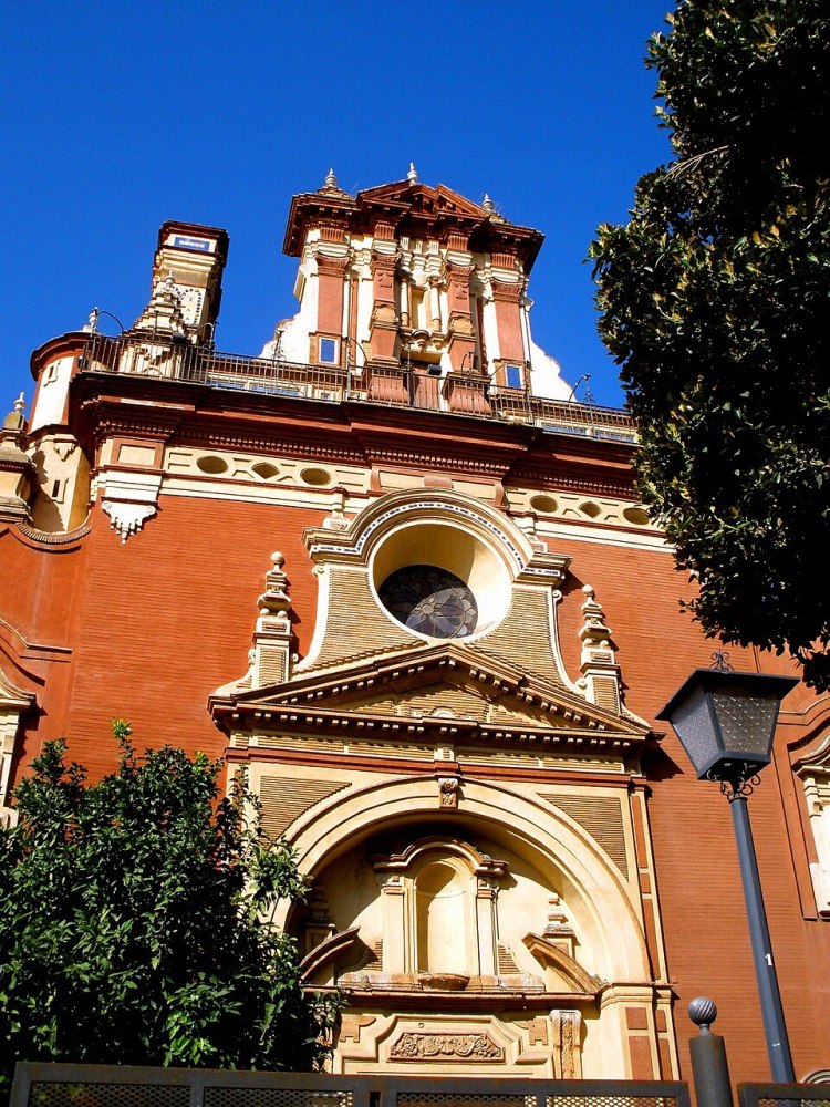 Ornate red brick building with a circular window and tower against a blue sky.