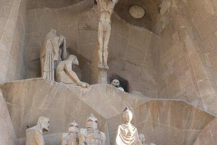 A vertical view of modernist stone sculptures at the Sagrada Familia, showing Jesus on the cross above and the Roman soldiers with Veronica's veil below.