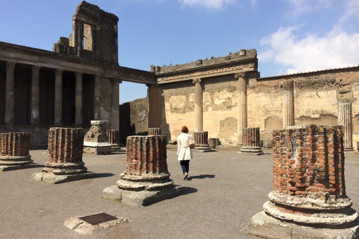 Person walking among the ancient ruins of pompeii with brick columns and a clear blue sky.