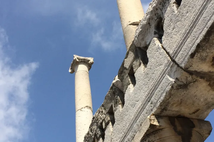 Ancient stone columns and arch against a blue sky with clouds.