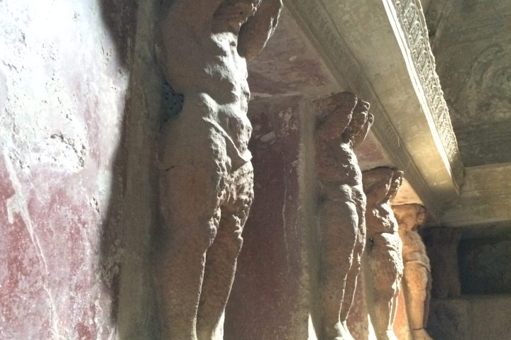 Stone statues of standing figures supporting ceiling in an ancient structure.