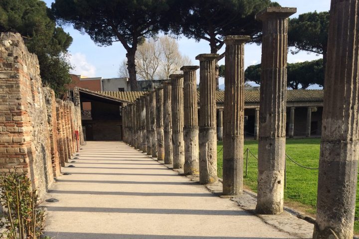 Stone columns line a pathway with grass and trees in the background.