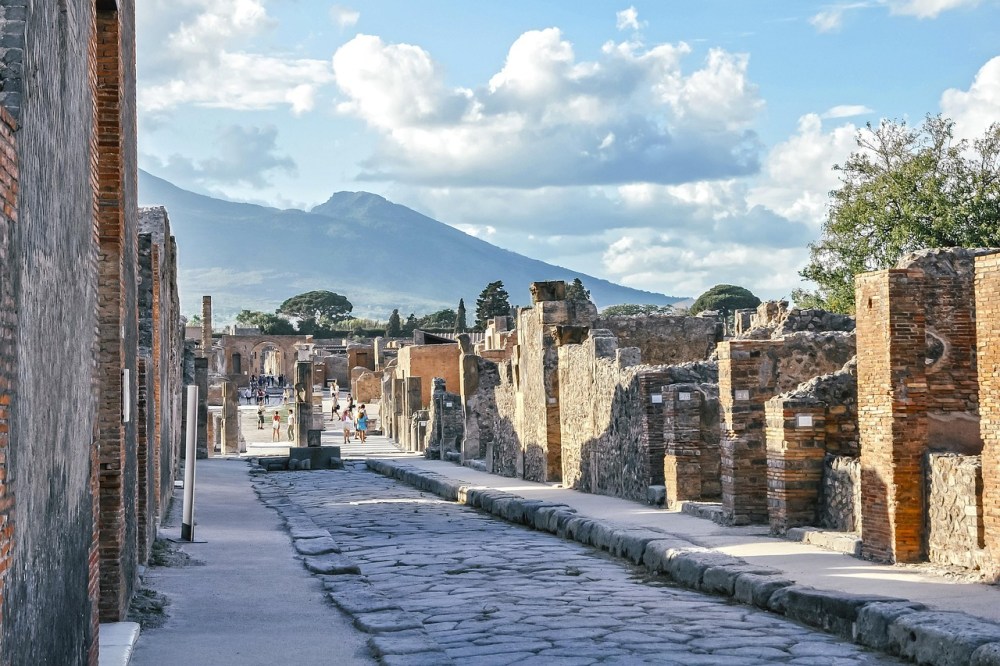 Ancient city of Pompeii guided tour: the city ruins with mount Vesuvius in the background, clear sky and scattered people walking.