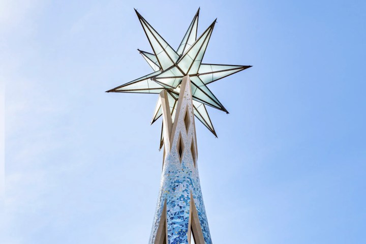 Tall, ornate spire with blue mosaic and star on top against a blue sky.