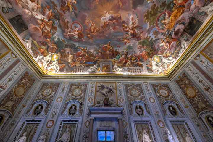 Ornate room with colorful painted ceiling depicting dramatic scenes and detailed wall carvings.