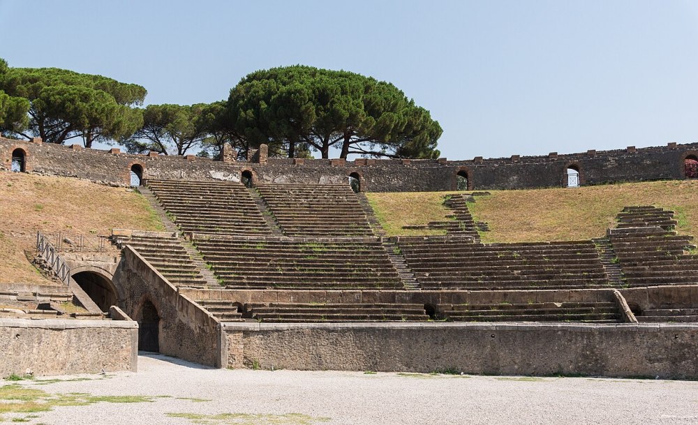 Ancient amphitheater with stone seating and trees in the background.