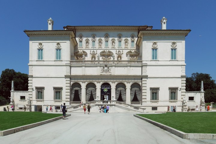 Grand classical building with statues and people walking outside on a sunny day.