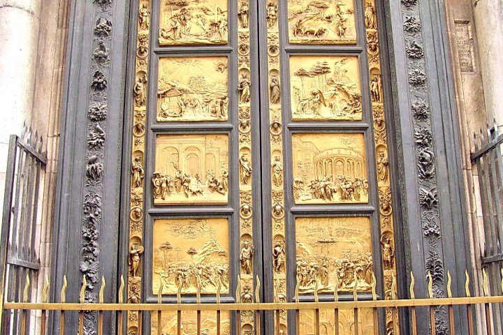 Elaborate gold doors with intricate carvings, framed by a dark border, behind a decorative metal fence.